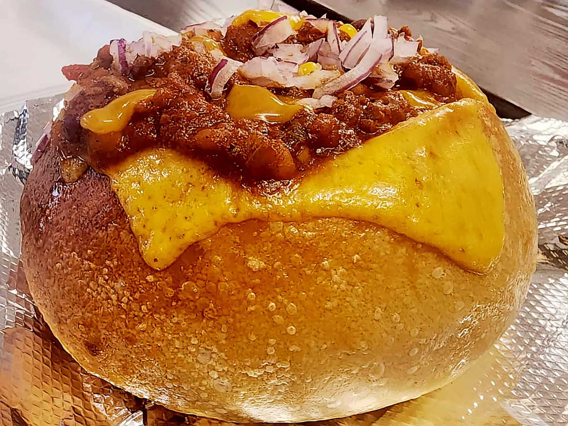Chili bread bowl topped with melted cheese and diced onions.