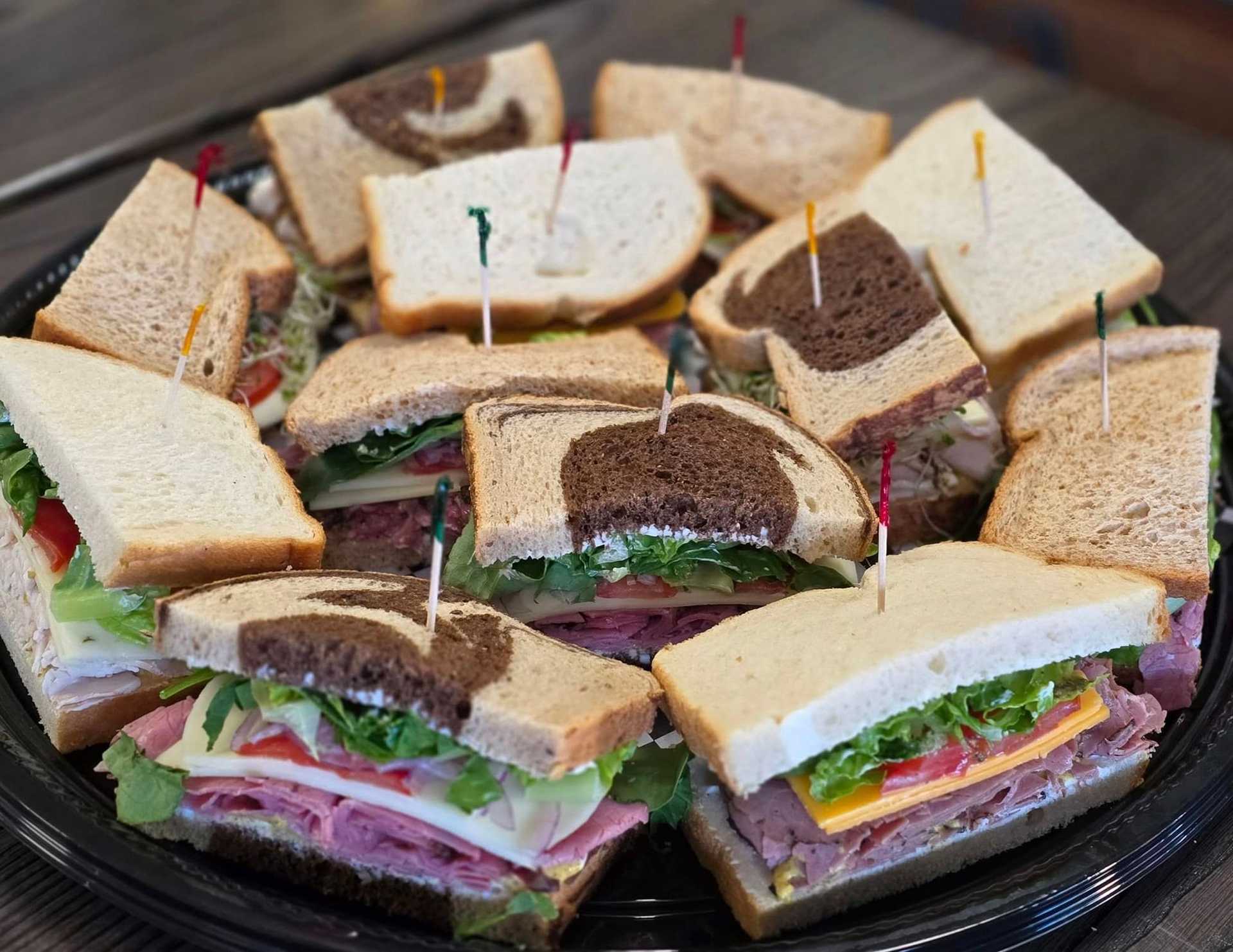 Assorted platter of deli sandwiches with various fillings and bread types.
